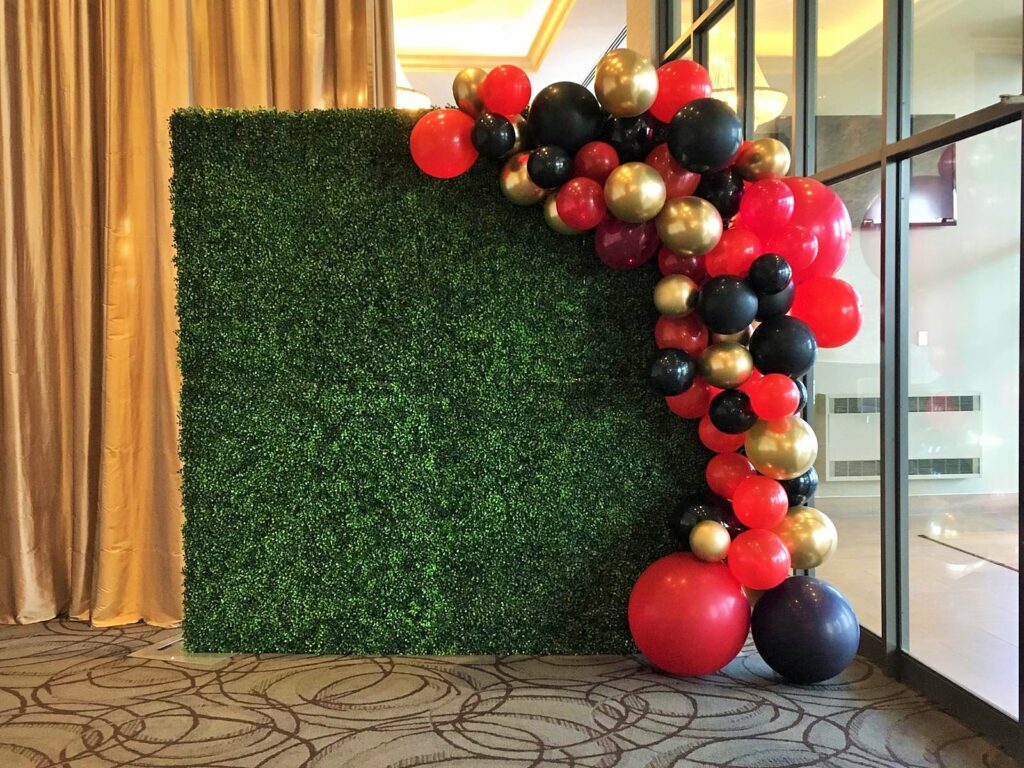 Balloon half arch decor service with green boxwood flower wall rental.